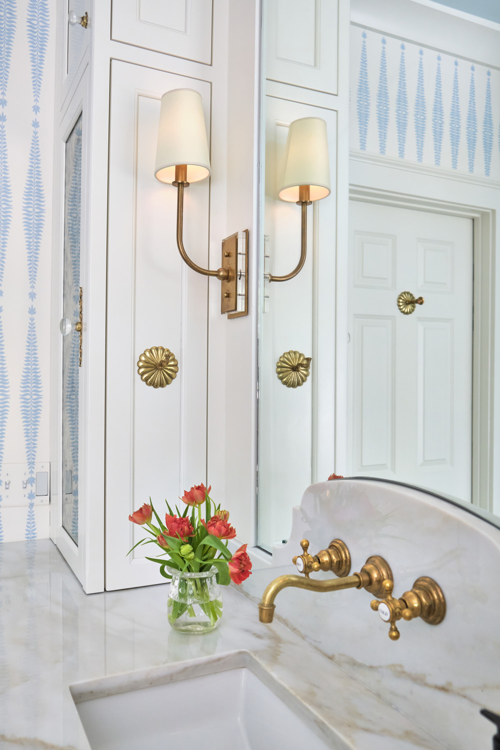 a detailed view of the brass sconce, marble countertop, and sink on one of the primary bathroom vanities