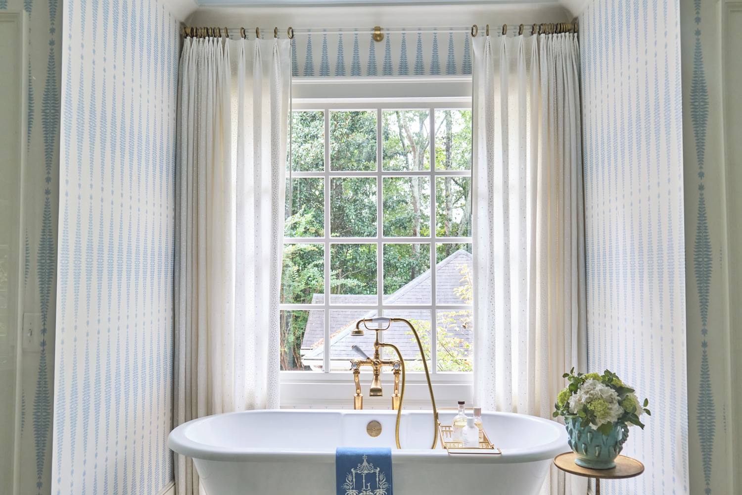 curtains with brass rod and blue and white patterned wallpaper draw the eye towards the classic tub