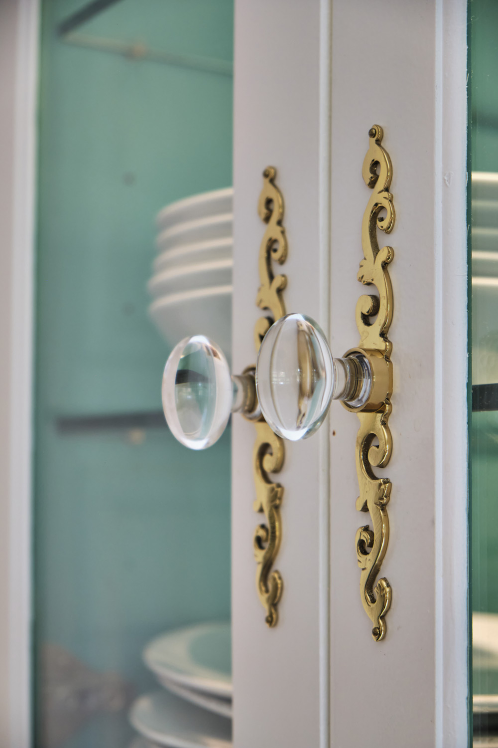 detail of the clear acrylic and gold knobs on the custom cabinetry with a peak at the teal color inside